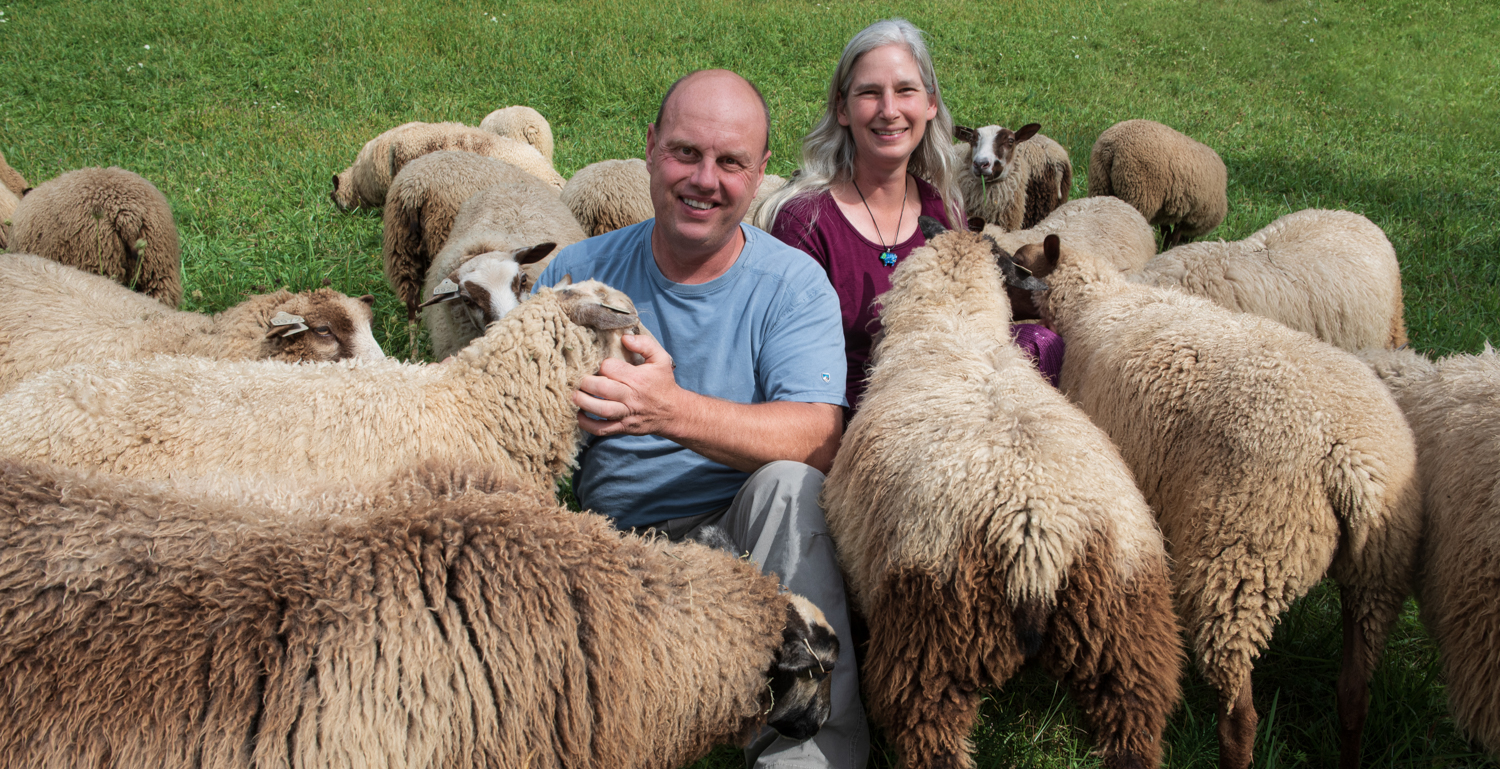 A man and woman sitting in front of some sheep at Point of View Farm